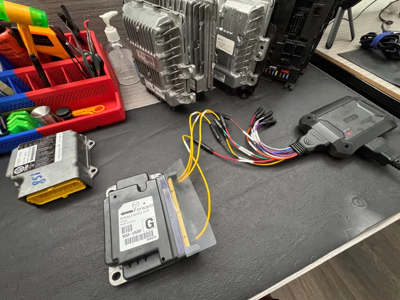 Mazda airbag module on SGTM workshop bench with connected wiring and diagnostic tool